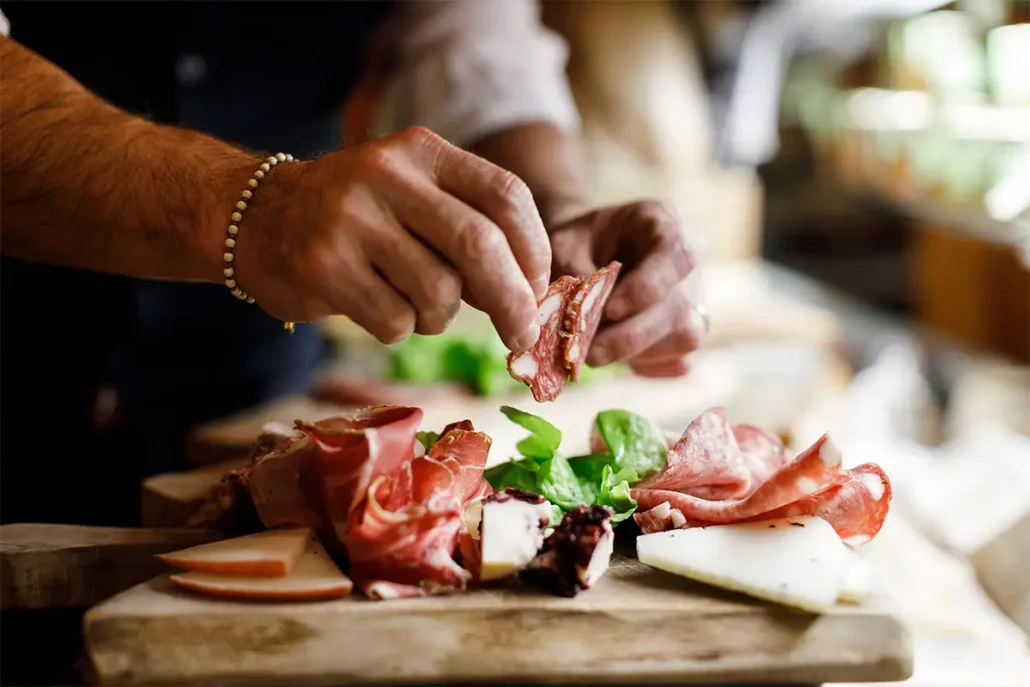 Hands preparing a Florentine charcuterie board with cured meats and fresh herbs during a food tour florence private and small groups tours - Florence Eat Parade Food Tour 1030x687 - Florence Private and Small Groups Tours