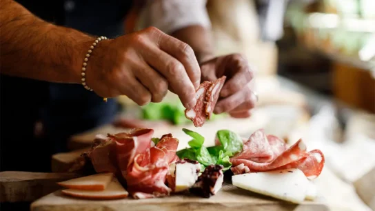 Hands preparing a Florentine charcuterie board with cured meats and fresh herbs during a food tour florentine eat parade - Florence Eat Parade Food Tour 544x306 - Florentine Eat Parade